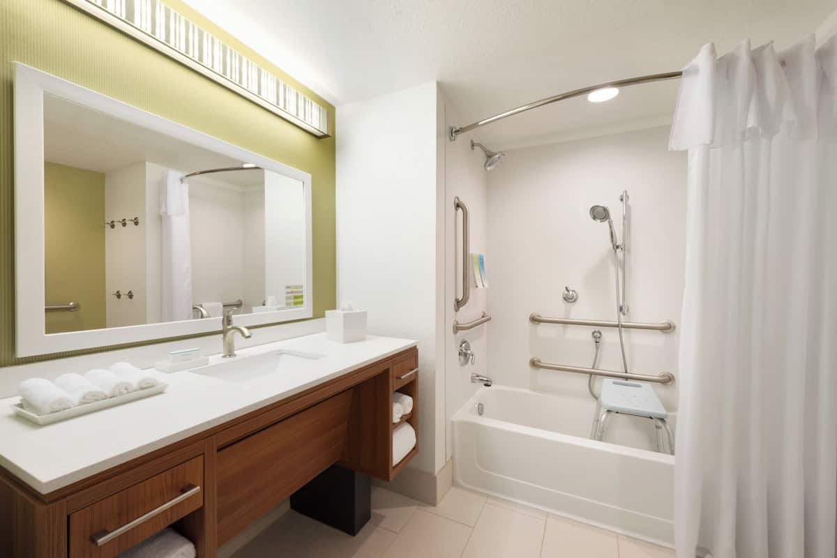 A modern bathroom with a large mirror, two sinks, a bathtub, and a shower with grab bars.