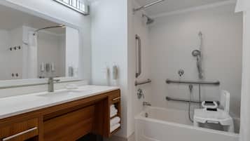 Un baño moderno con un espejo grande, lavamanos blanco, tocador de madera y ducha a ras de suelo con barra de apoyo.