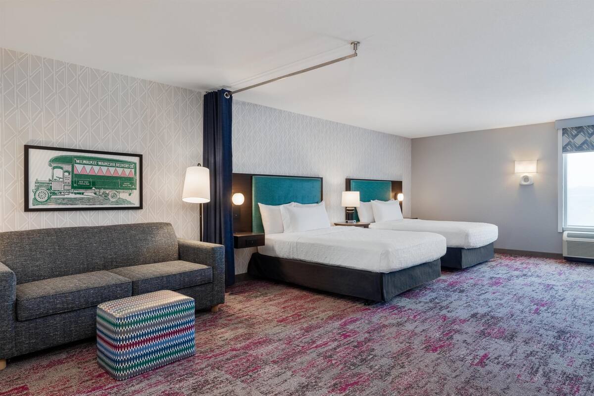 A hotel room with two beds, a sofa, a patterned rug, and a framed picture on the wall.