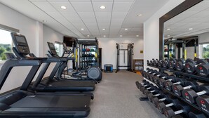 Une salle de sport équipée de tapis de course, d’appareils de musculation et d’un porte-haltères.