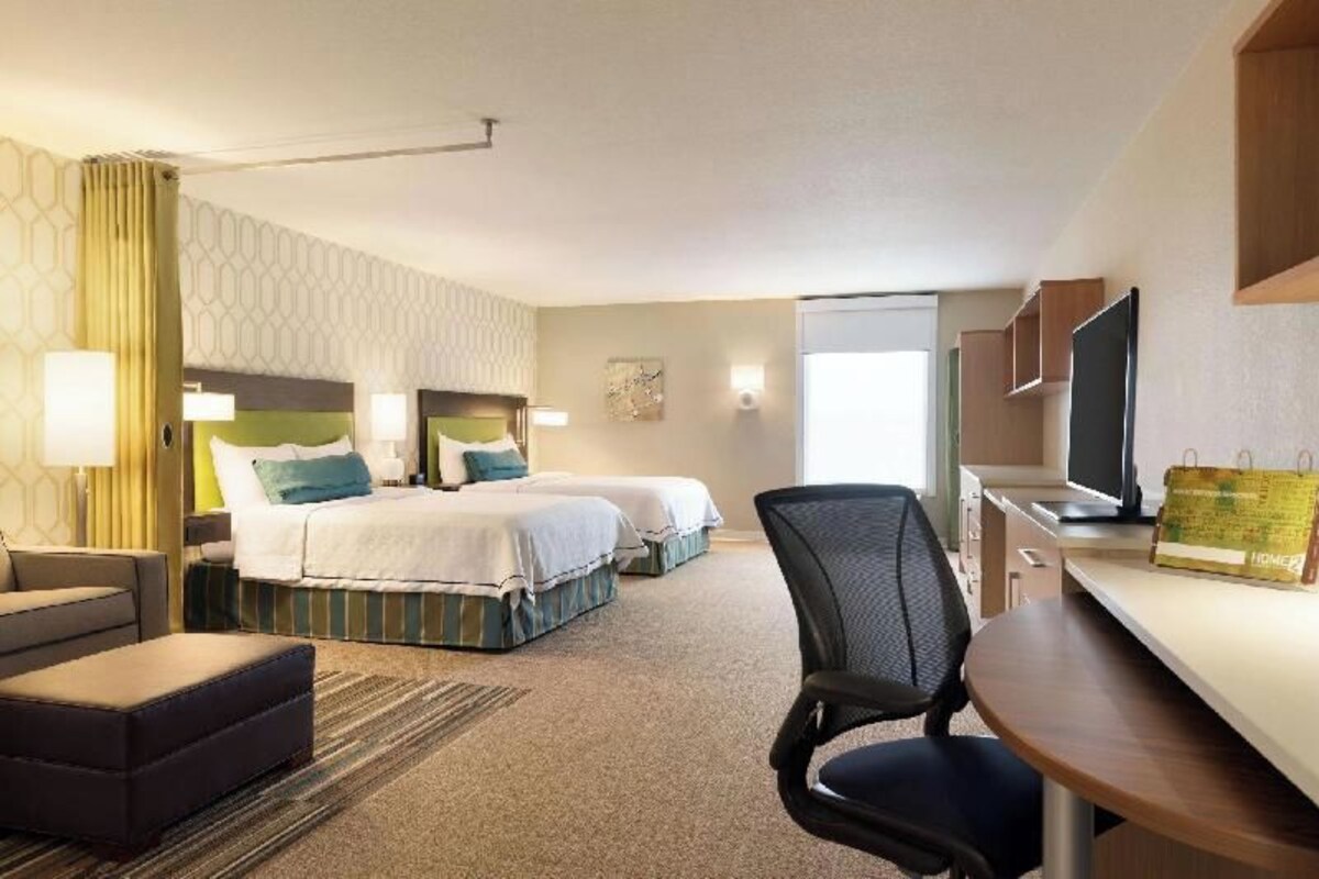 Habitación de hotel con dos camas, un escritorio, una silla, un televisor y una ventana.