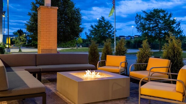 Un espace extérieur aménagé avec un foyer, des canapés et des fauteuils, le tout abrité par une structure couverte sur laquelle est installé un mât pour drapeau.