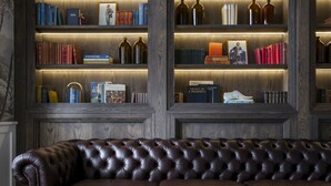 A dark brown leather sofa in front of wooden shelves with books and decorative bottles. - Harpers House (Cape Town)