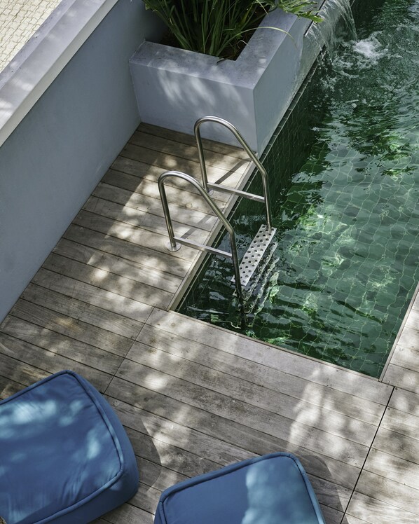 Una terraza de madera con una escalera de metal que da a una piscina transparente.