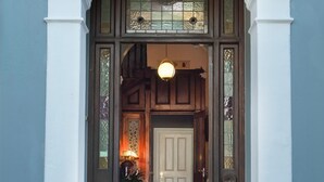 A grand entrance with a white archway, a wooden door, and a patterned rug leading to a tiled floor. - Harpers House (Cape Town)