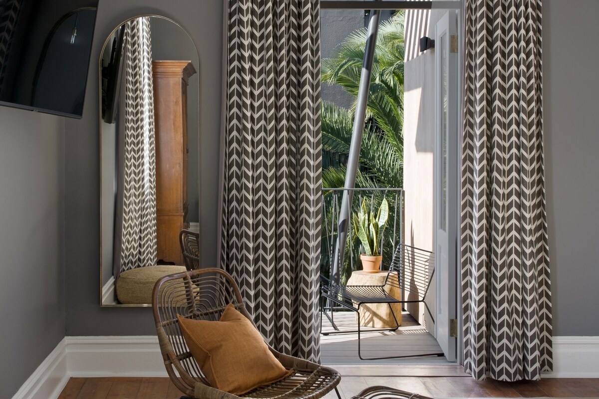 A modern living room with a large mirror, a wicker chair, a small table, and a potted plant.