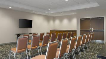 Une salle de conférence avec des rangées de chaises, un téléviseur à écran plat, un pupitre et une porte.