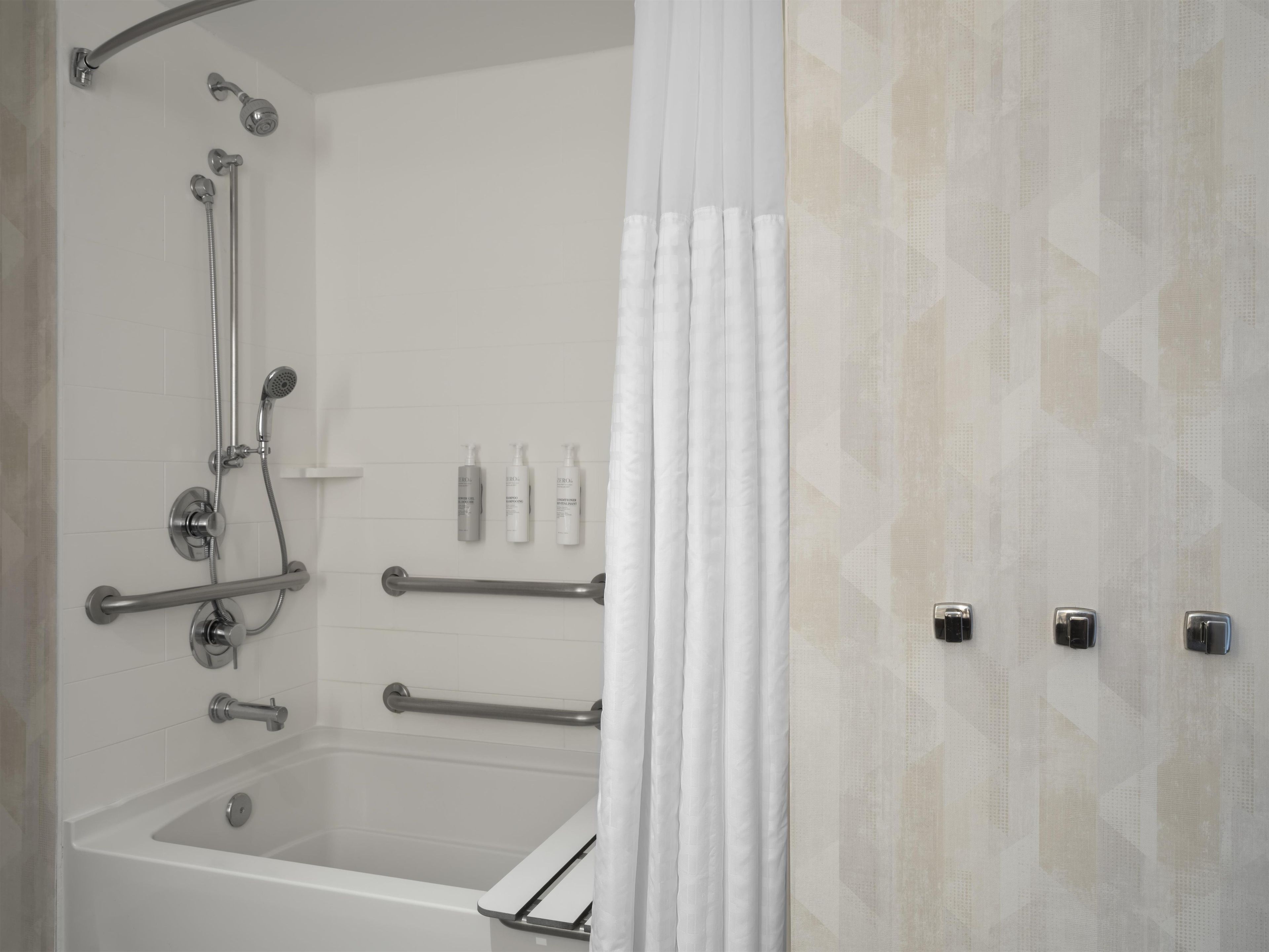 Une salle de bain équipée d’une baignoire, d’une douche, de barres d’appui et d’un porte-serviettes.