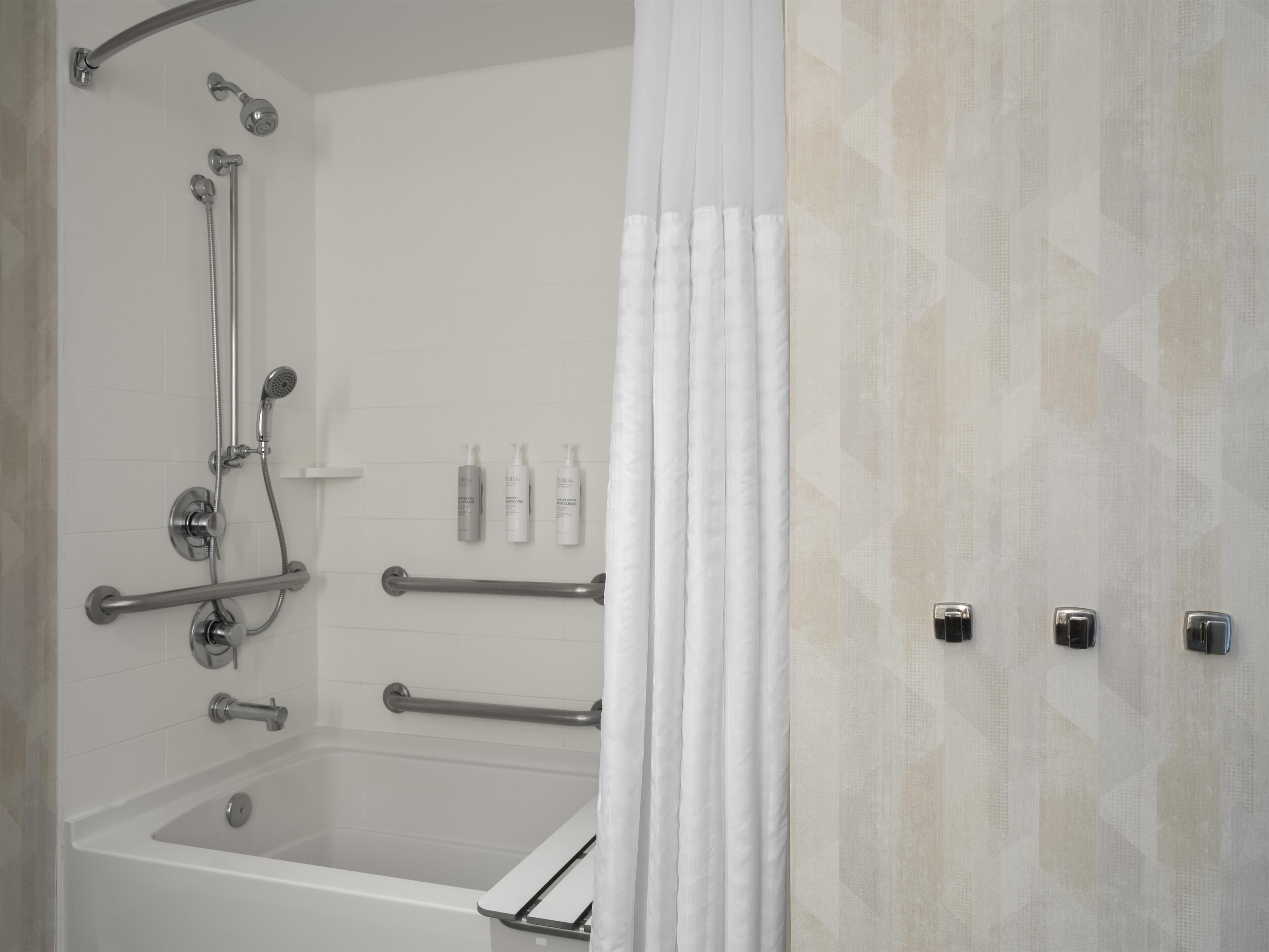 Un baño con bañera, ducha, barras de apoyo y un perchero para toallas.