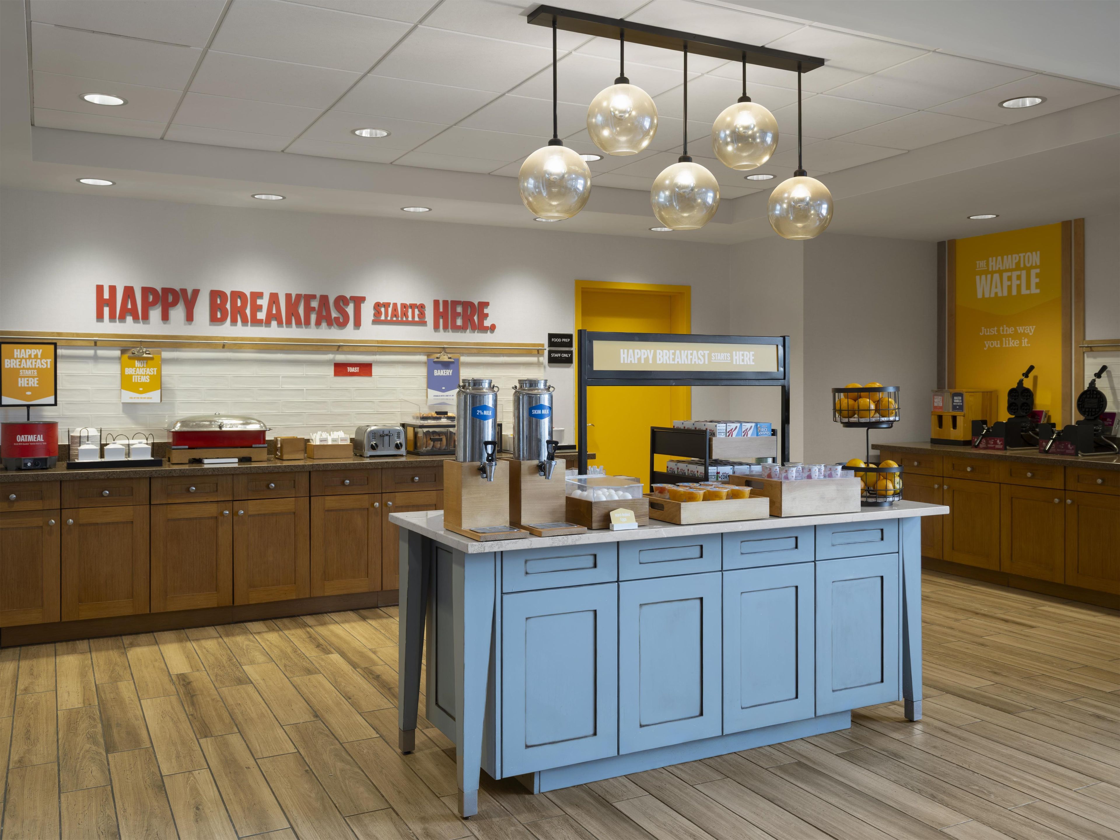 A breakfast area with a sign reading 'HAPPY BREAKFAST STARTS HERE,' a coffee station, and a waffle maker display.