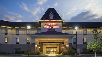 A hotel with a prominent sign reading 'Hampton Inn & Suites,' featuring a modern architectural style with a stone facade and a symmetrical design.