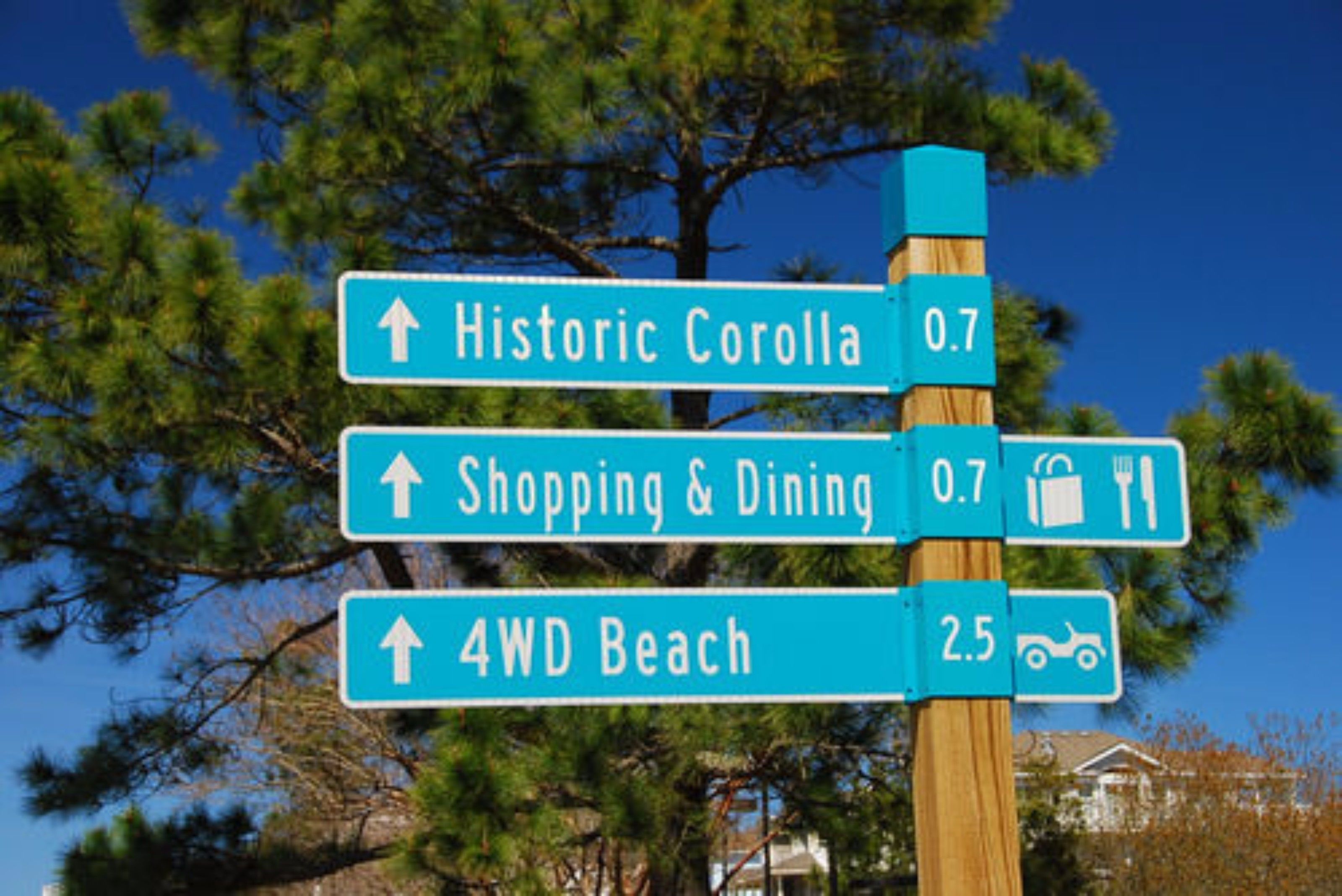 A directional sign with arrows pointing to Historic Corolla, Shopping & Dining, and 4WD Beach.