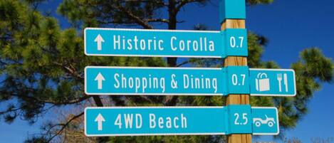 A directional sign with arrows pointing to Historic Corolla, Shopping & Dining, and 4WD Beach.