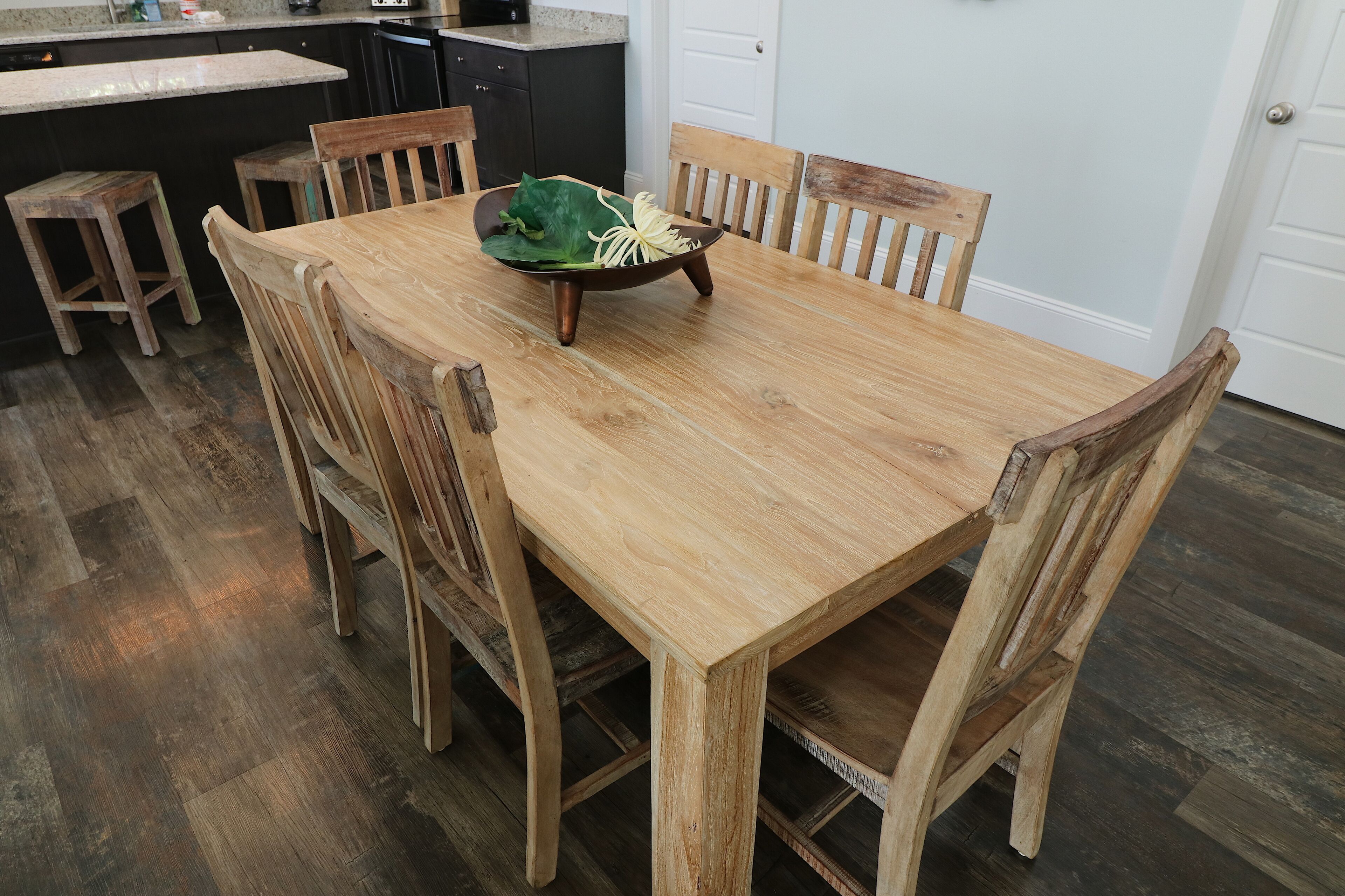 A wooden dining table with chairs, a bowl of food, and a kitchen in the background.