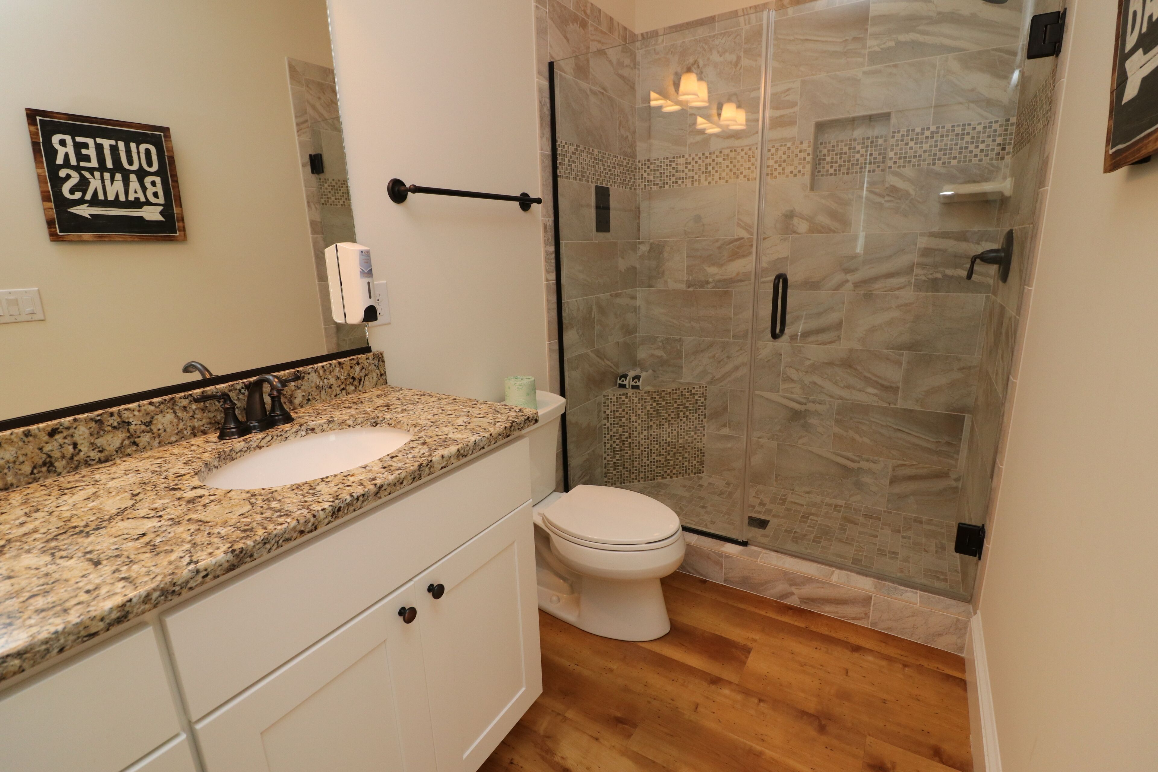 Un baño con lavamanos de granito, inodoro y ducha con mampara de vidrio y pared azulejada.
