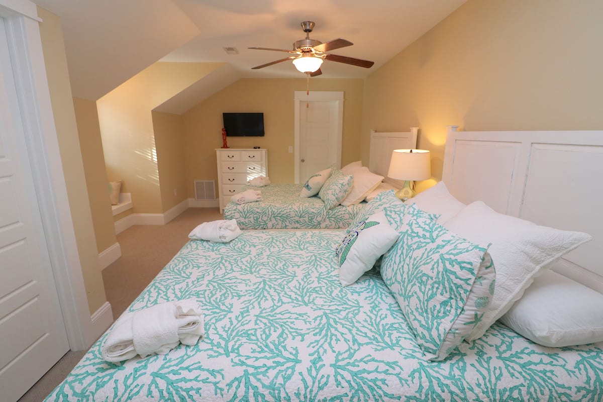Une chambre avec deux lits, un ventilateur de plafond, une télévision et une commode.
