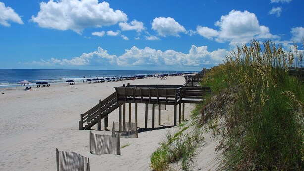 A beach with a wooden walkway leading to the water, sandy beach, and a clear blue sky.
