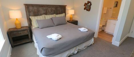 A neatly made bed with a grey and white duvet, two bedside lamps, and a wooden headboard.