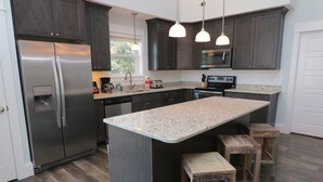 A modern kitchen with dark cabinets, stainless steel appliances, a granite countertop, and wooden stools.
