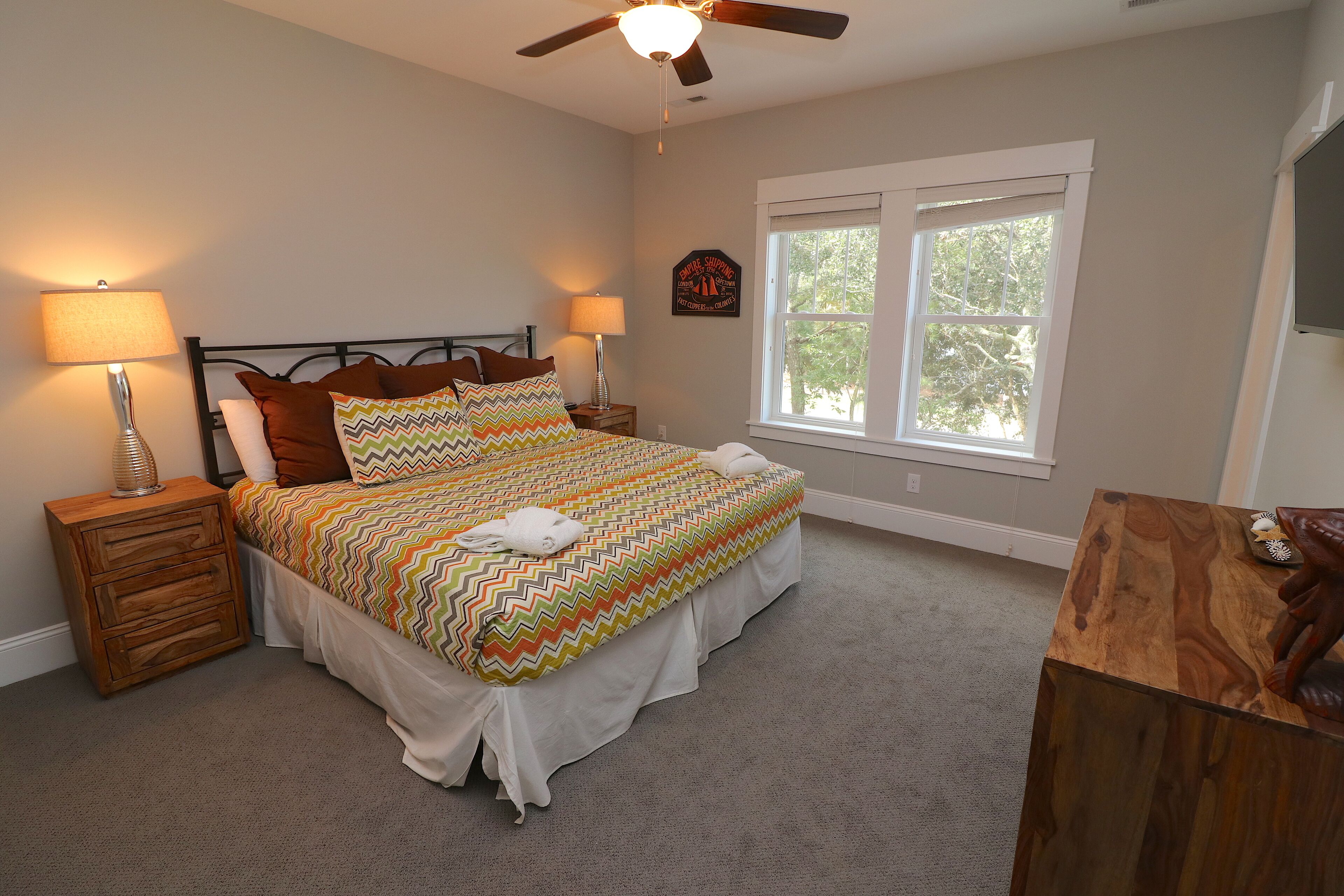 A bedroom with a bed, two bedside tables, a ceiling fan, a window, and a wall-mounted decoration.