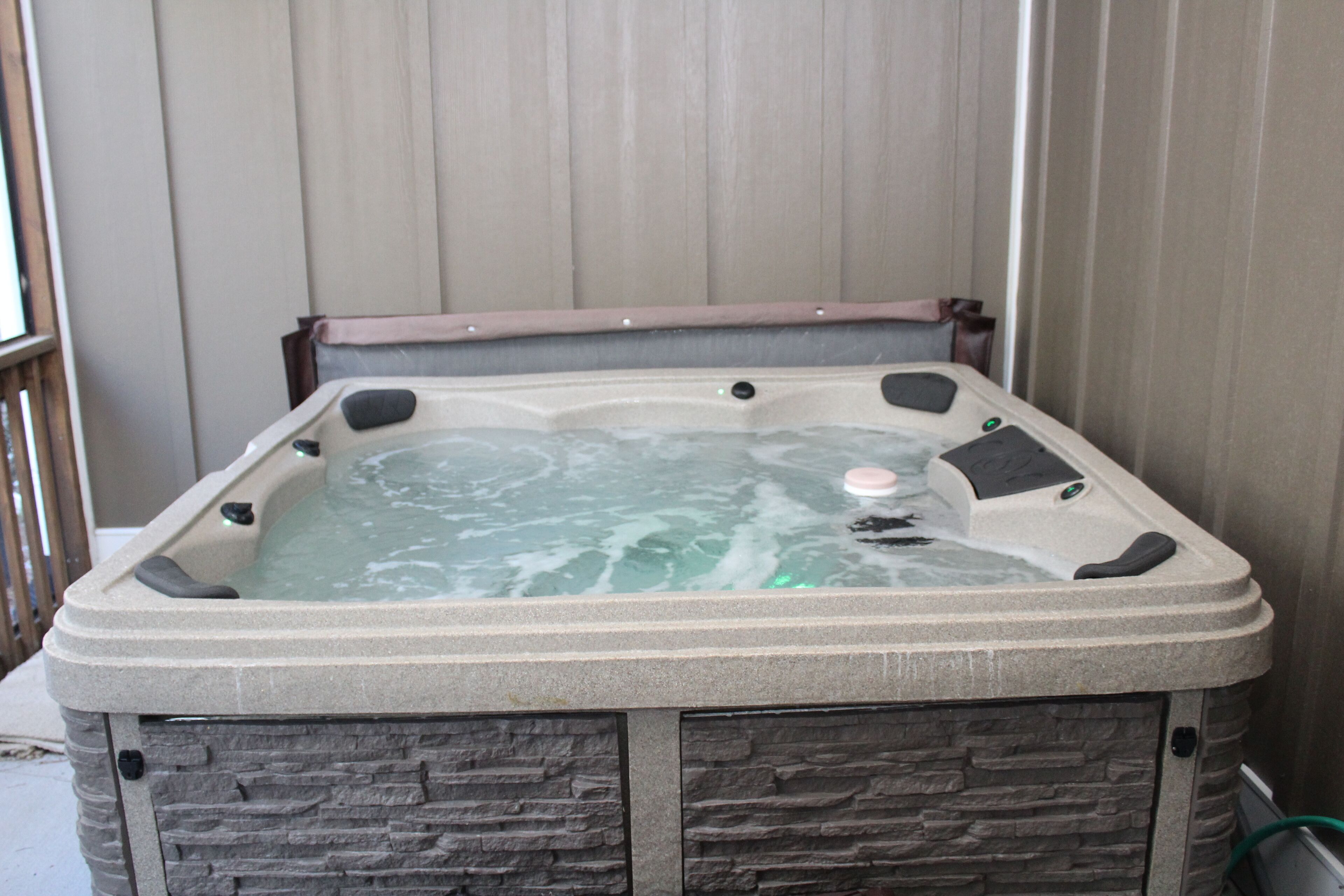 A hot tub with stone-like exterior and a wooden bench.