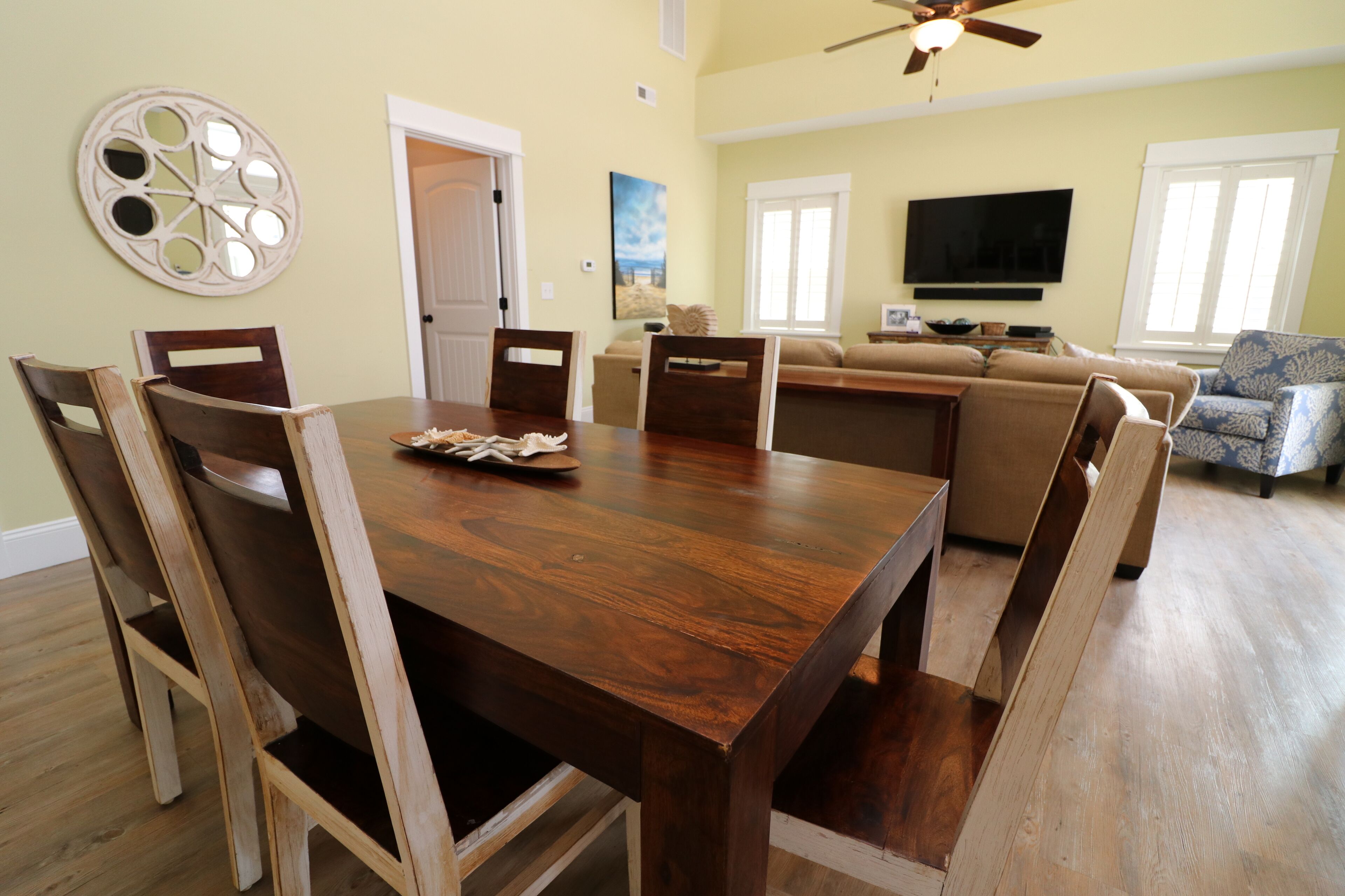 A dining area with a wooden table and chairs, a sofa, and a television in the background.