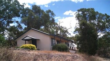 A single-story house with a gabled roof, surrounded by trees and dry grass.