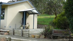 A building with a covered porch, a wooden fence, and a bench. - Riesling Country Cottages (Polish Hill River)