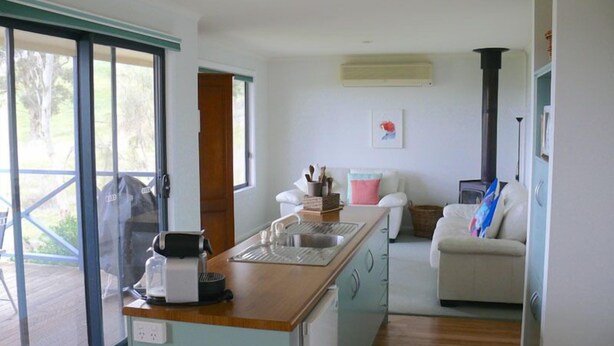 A compact kitchen with a coffee maker, sink, and a small island. There is a sofa and a fireplace in the living area. - Riesling Country Cottages (Polish Hill River)