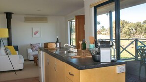 A modern kitchen with a large island, a dining area with a view, and a cozy living space with a sofa and a lamp. - Riesling Country Cottages (Polish Hill River)