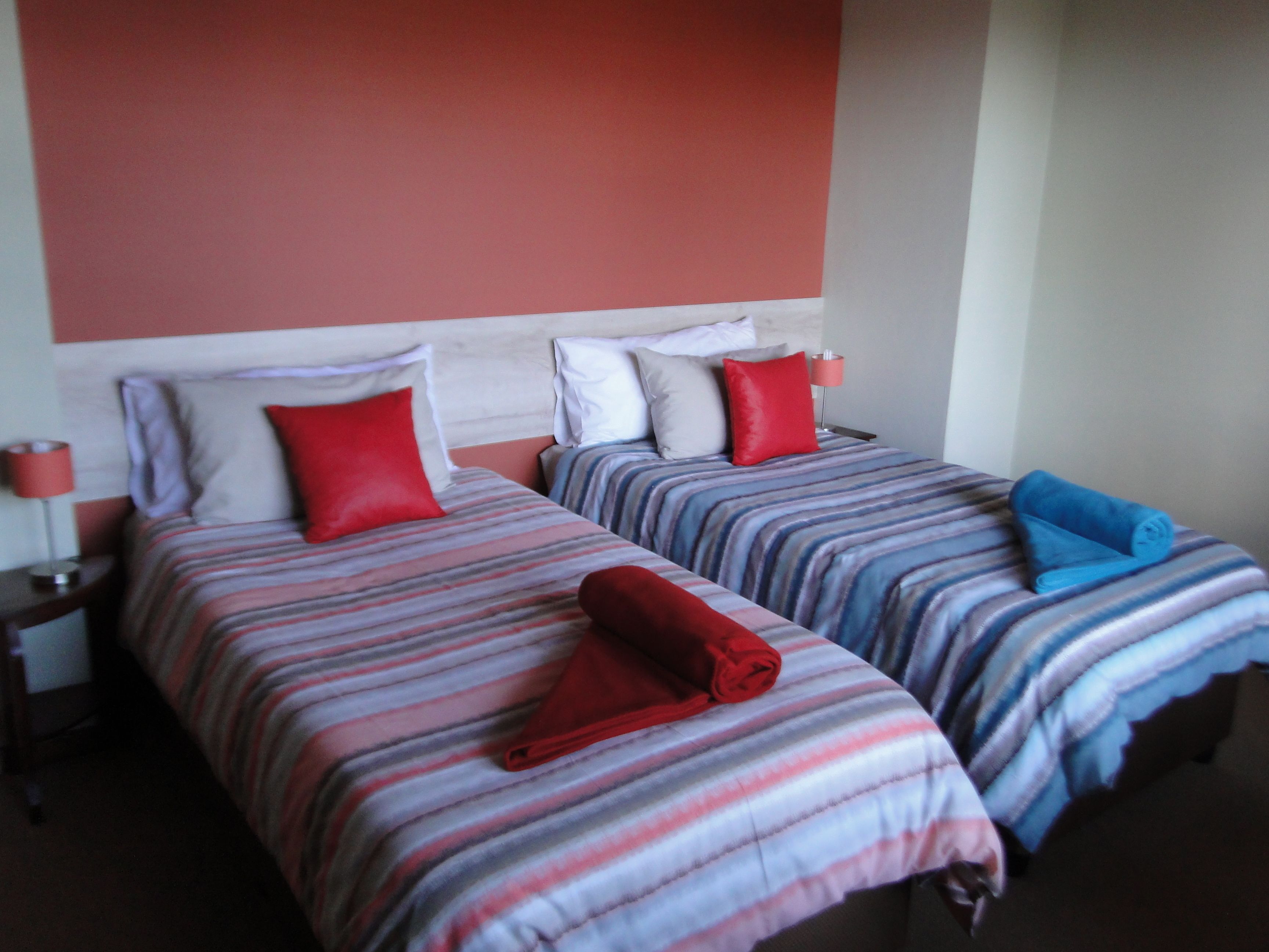 Two single beds with striped bedding, red and blue towels, and bedside lamps.