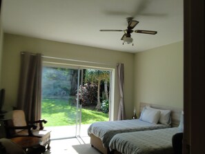 A bedroom with a bed, a chair, a ceiling fan, and a sliding glass door leading to a garden. - Bluewater Beach Accommodation (Gqeberha (Port Elizabeth))
