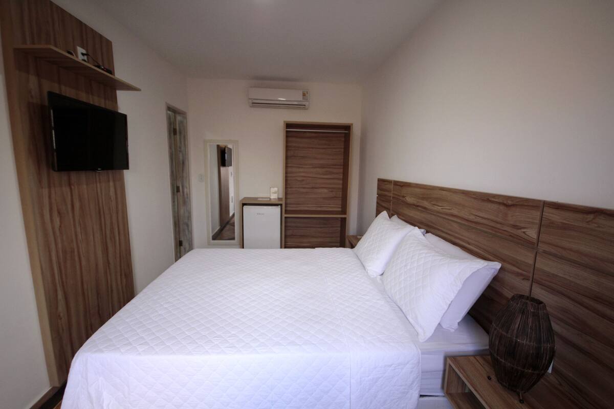 A bedroom with a bed, a television, a wardrobe, and a mirror.