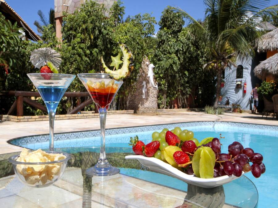 Escena junto a la piscina con dos vasos de martini, un cuenco de patatas fritas y una fuente de fruta.