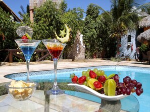 Escena junto a la piscina con dos vasos de martini, un cuenco de patatas fritas y una fuente de fruta.