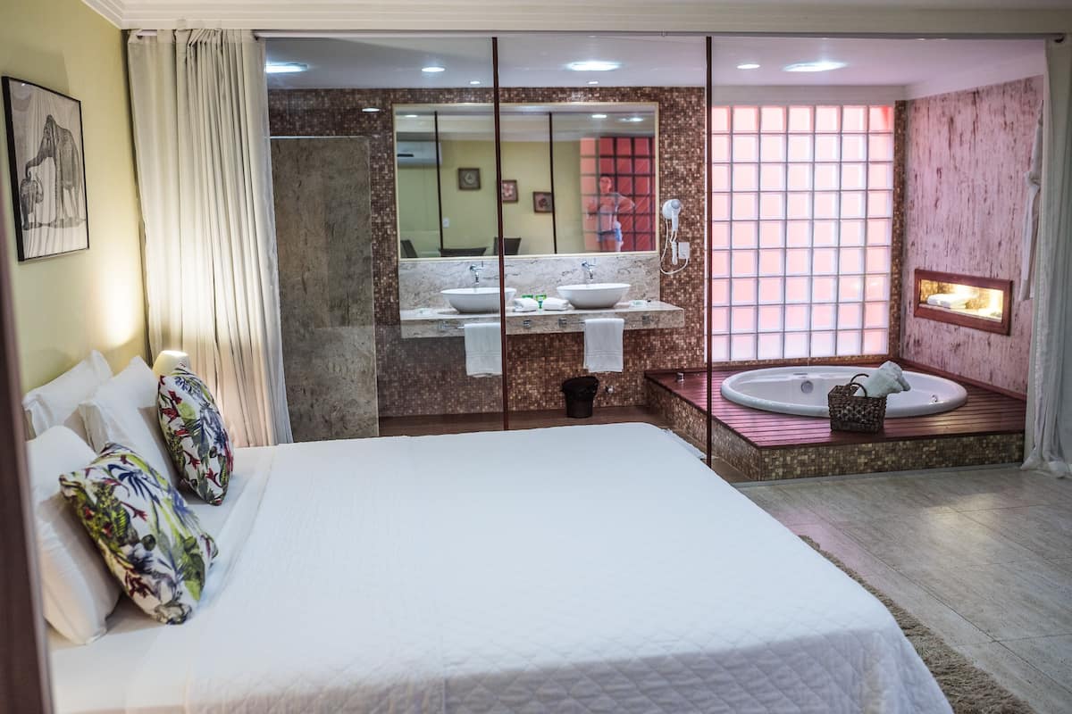 A hotel room with a large bed, two bathrooms with sinks, a bathtub, and a large mirror.