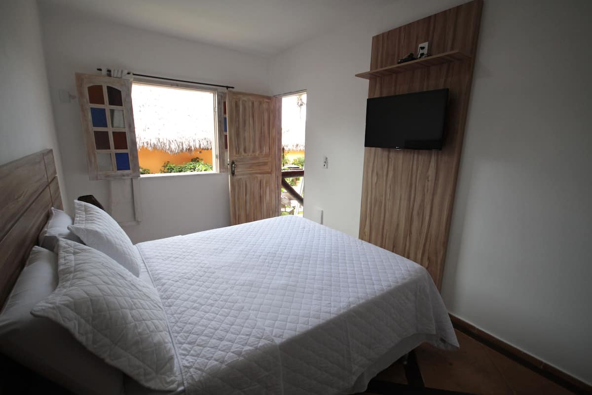 A bedroom with a bed, a TV mounted on the wall, and a window with curtains.