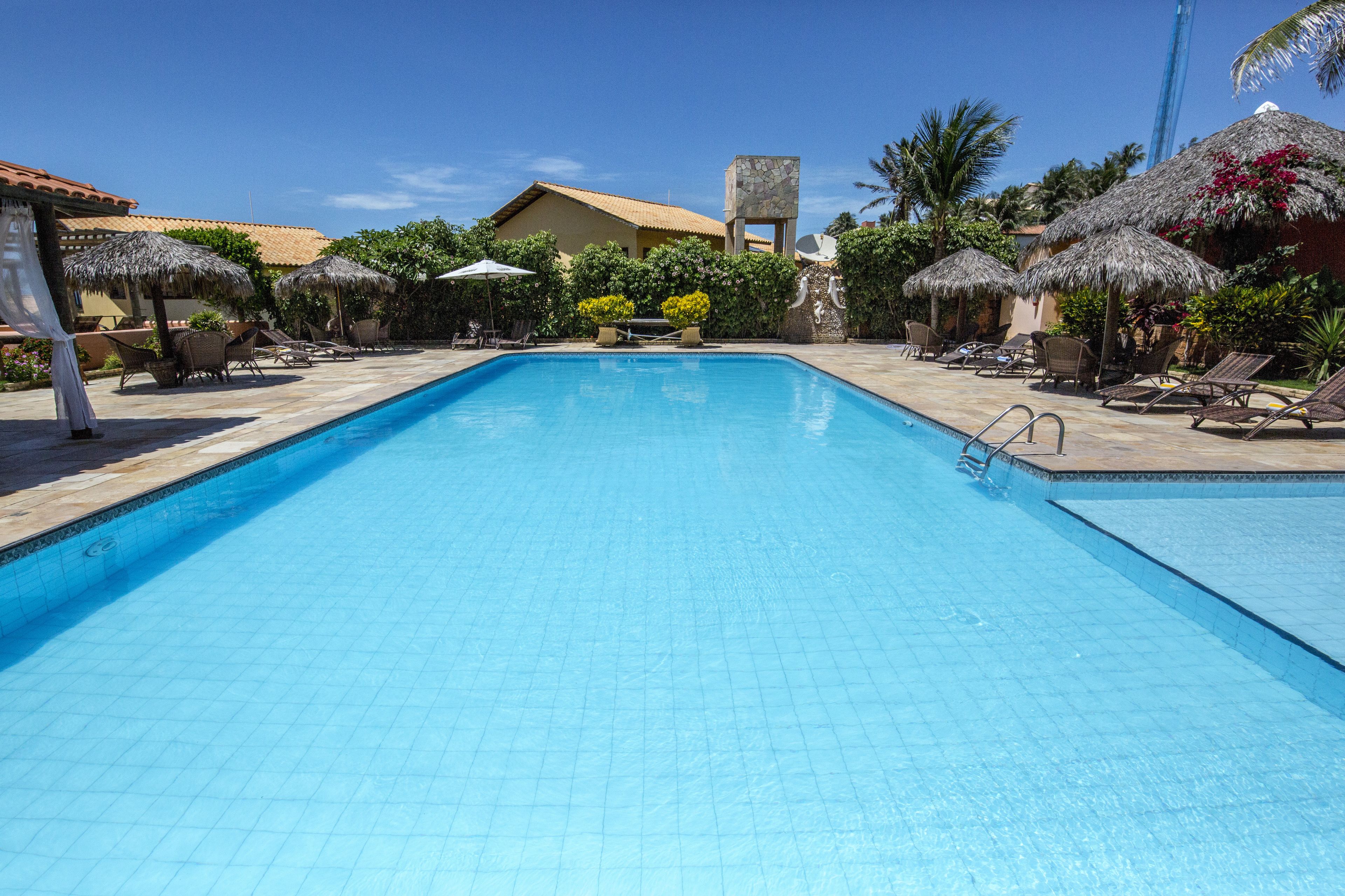 Una piscina con sillas de descanso y sombrillas, rodeada de edificios y vegetación.