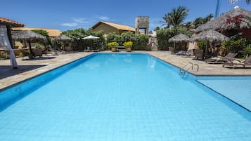 Una piscina con sillas de descanso y sombrillas, rodeada de edificios y vegetación.