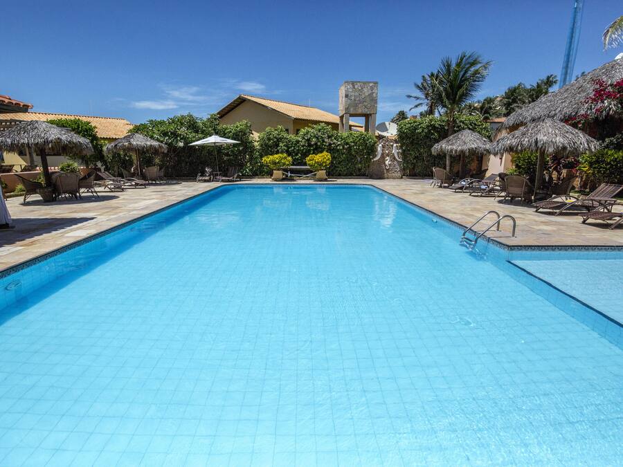 Una piscina con sillas de descanso y sombrillas, rodeada de edificios y vegetación.