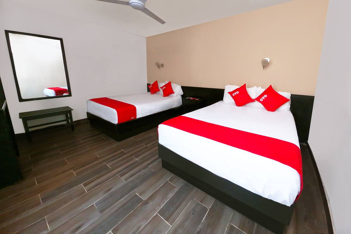 Una habitación de hotel con dos camas, un ventilador de techo, un espejo grande y suelo de madera.
