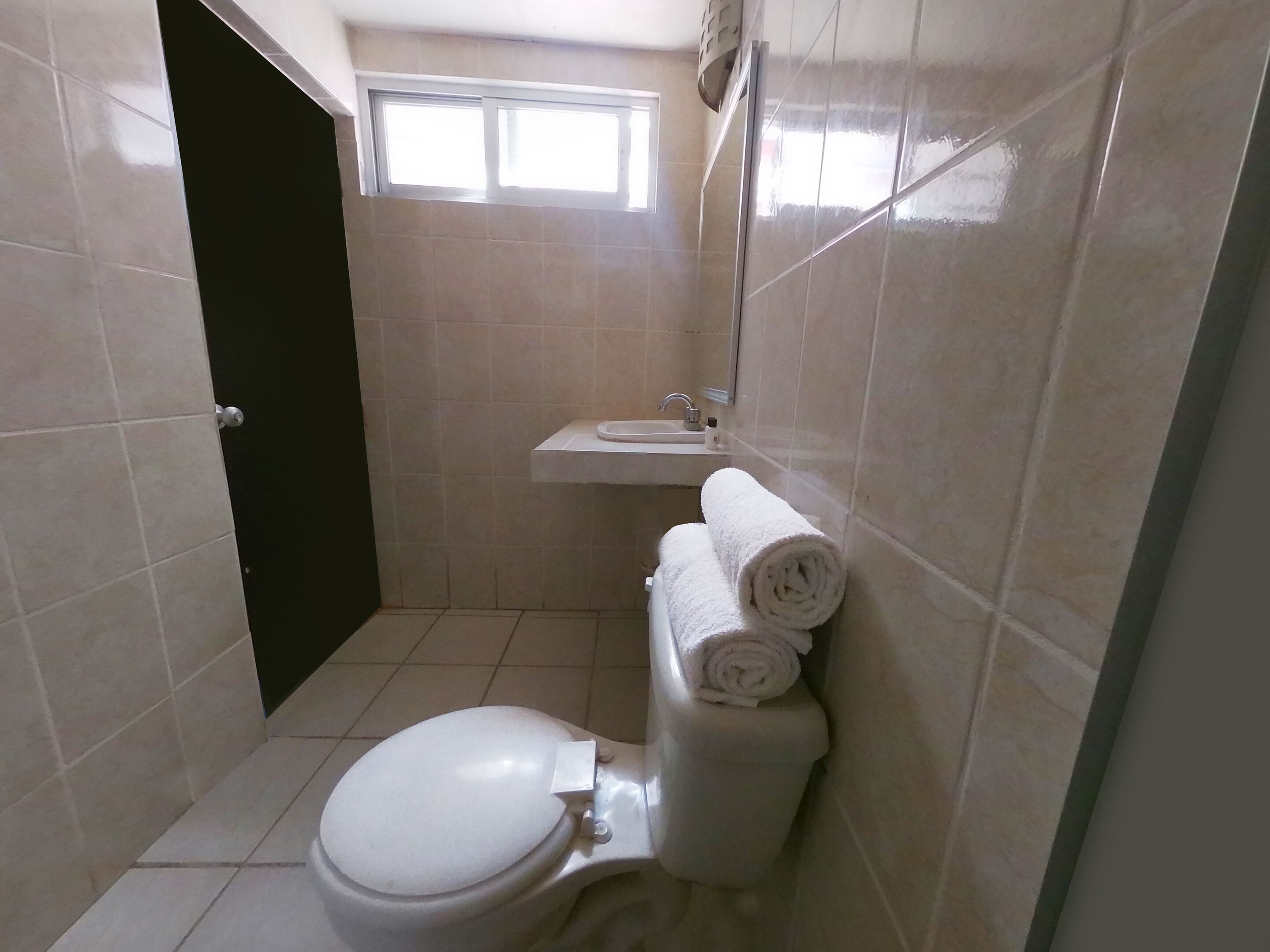 A small, clean bathroom with a toilet, a sink, and a mirror. There are two rolled towels on the wall.