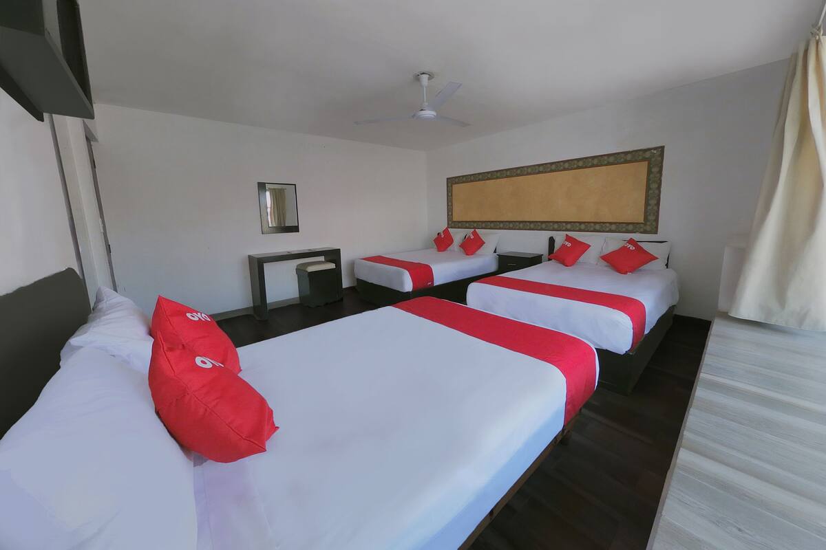 Habitación de hotel con dos camas individuales, un escritorio, una silla, un ventilador de techo y un espejo grande.