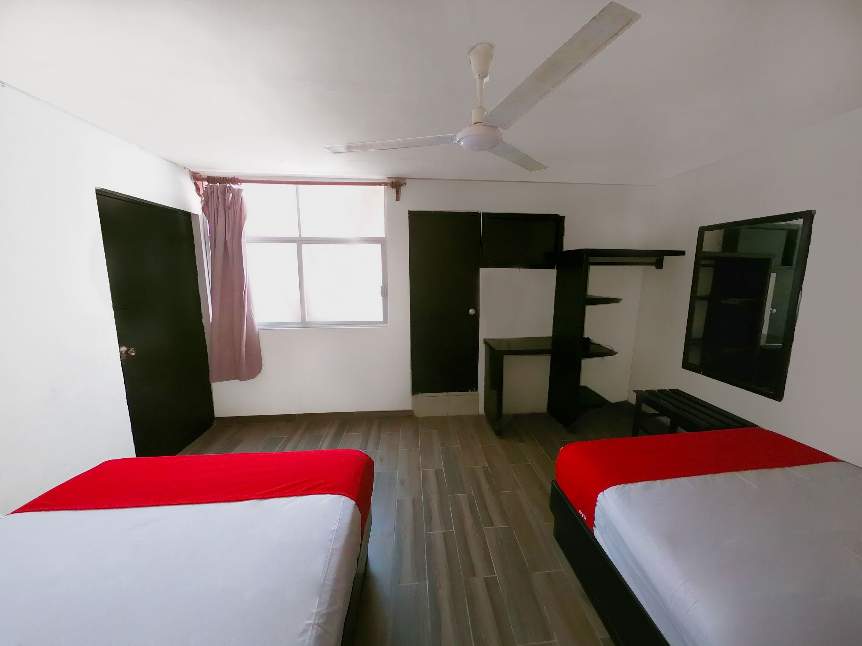 A room with two beds, a ceiling fan, a window with curtains, a desk, and a mirror.
