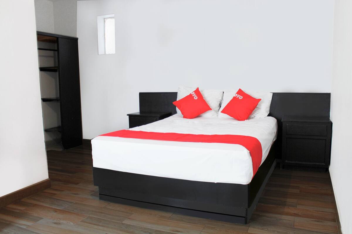 Una cama bien hecha con una colcha blanca y roja, dos mesitas de noche y un piso de madera.