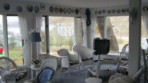 A sunroom with wicker furniture, a television, and decorative plates on the walls. - The Olde Village Inn (Sandy Cove)