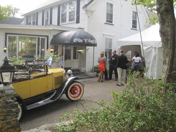 A vintage car parked in front of a building with a tent and people gathered around. - The Olde Village Inn (Sandy Cove)