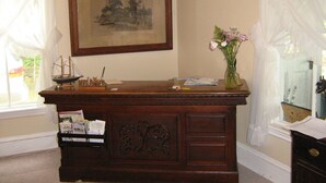 A wooden desk with a ship model, a framed landscape painting, and a vase with flowers. - The Olde Village Inn (Sandy Cove)