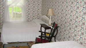 A bedroom with floral wallpaper, a bed, a chair, and a lamp. - The Olde Village Inn (Sandy Cove)