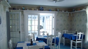 A dining area with white tables and chairs, blue tablecloths, and a view through a glass door. - The Olde Village Inn (Sandy Cove)